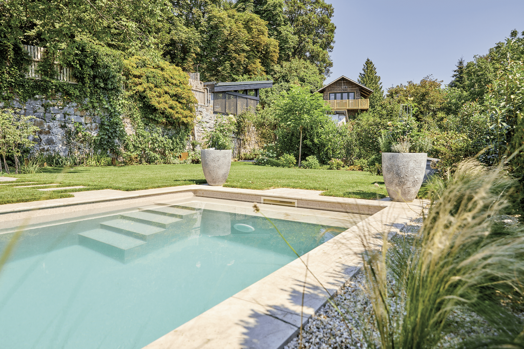 Friedrich Reitinger Schwimmbad und Wellness zeigt einen sehr natürlich gehaltenen Garten mit vielen Pflanzen und einem in den Boden eingelassenen, rechteckigen Pool mit Stufen und gefliester Umrandung.