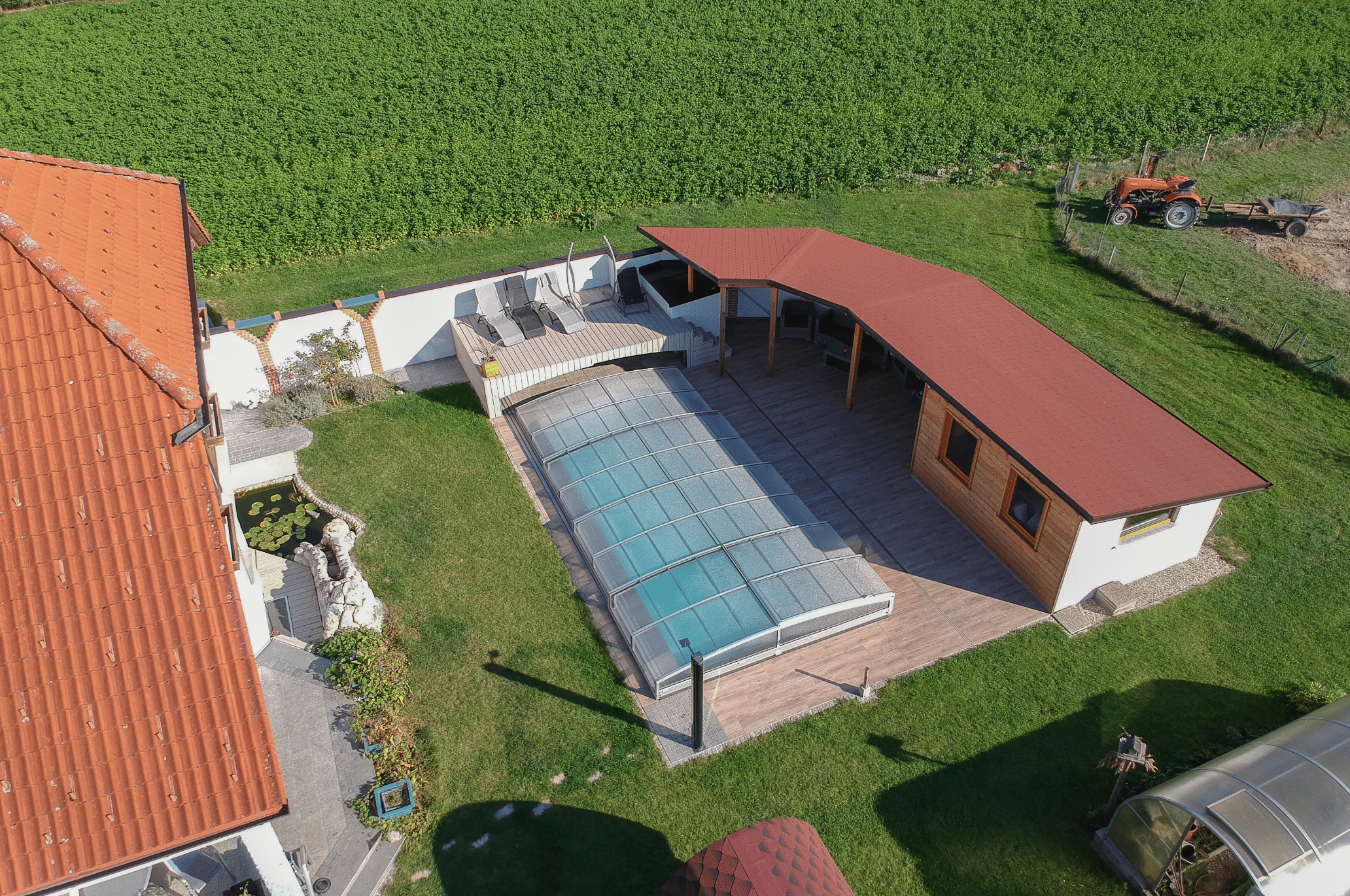 Friedrich Reitinger Schwimmbad und Wellness zeigt einen in den Boden eingelassenen, rechteckigen Pool mit einer Poolüberdachung aus Glas in einem schönen Innenhof mit Sonnendeck und Gartenteich.