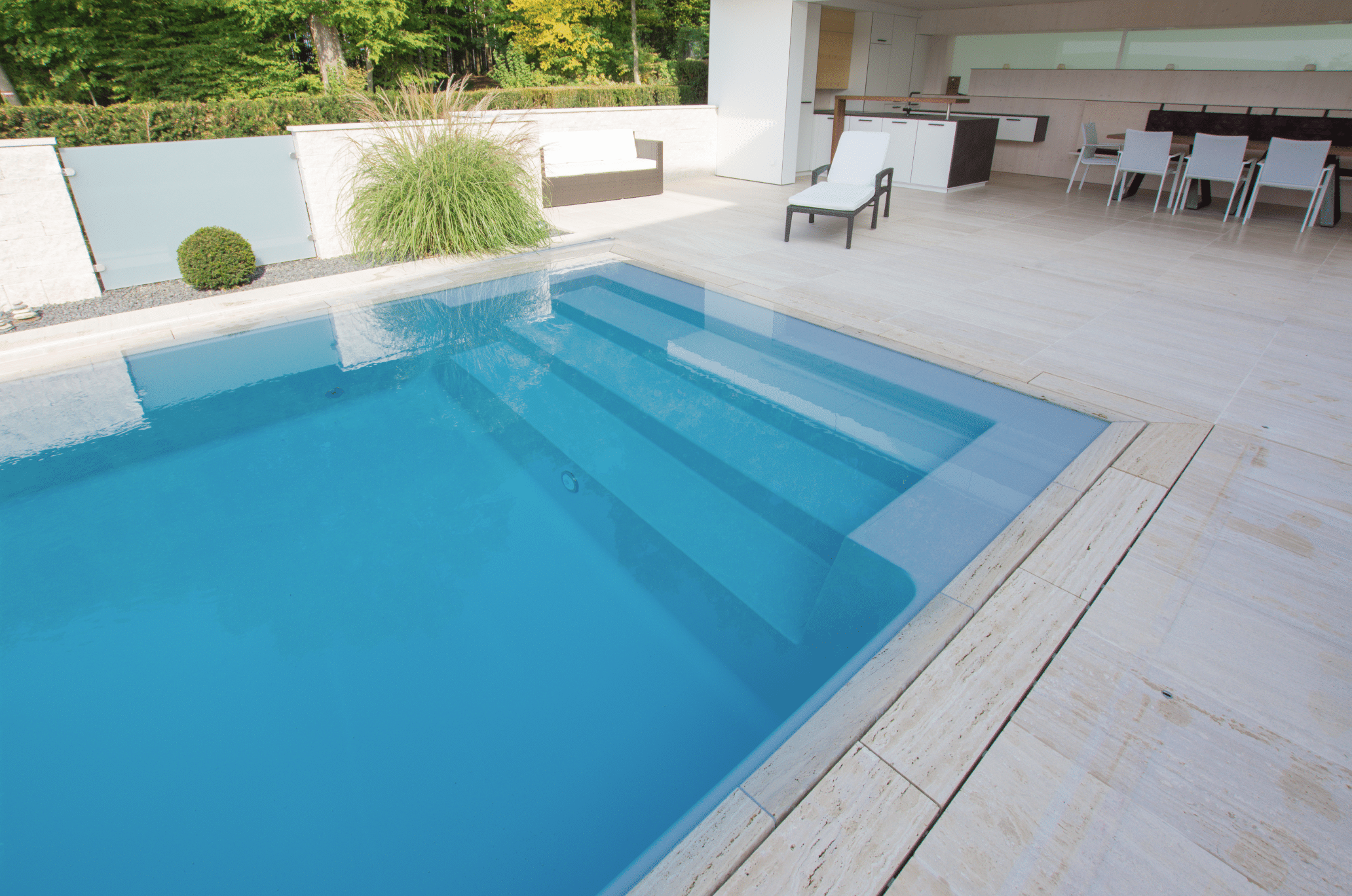 Friedrich Reitinger Schwimmbad und Wellness zeigt einen in den Boden eingelassenen, rechteckigen Pool auf einer gefliesten Terrasse mit Überdachung und einer Sitzgruppe.