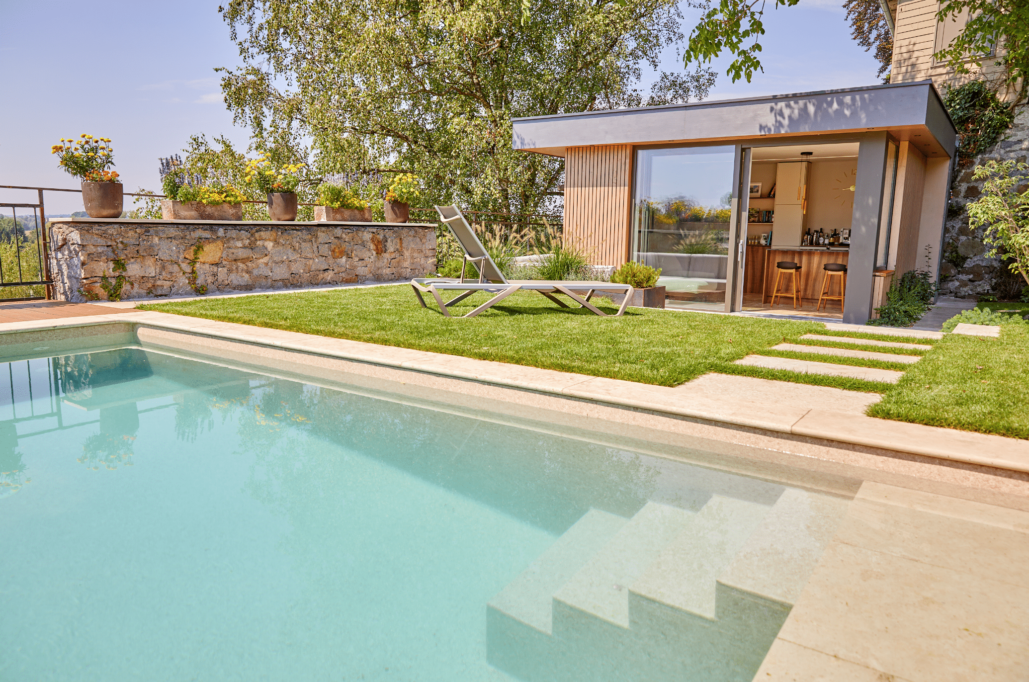 Friedrich Reitinger Schwimmbad und Wellness zeigt einen in den Boden eingelassenen, rechteckigen Pool in einem schönen Garten mit einer Gartenhütte und Sonnenliegen auf dem Rasen.