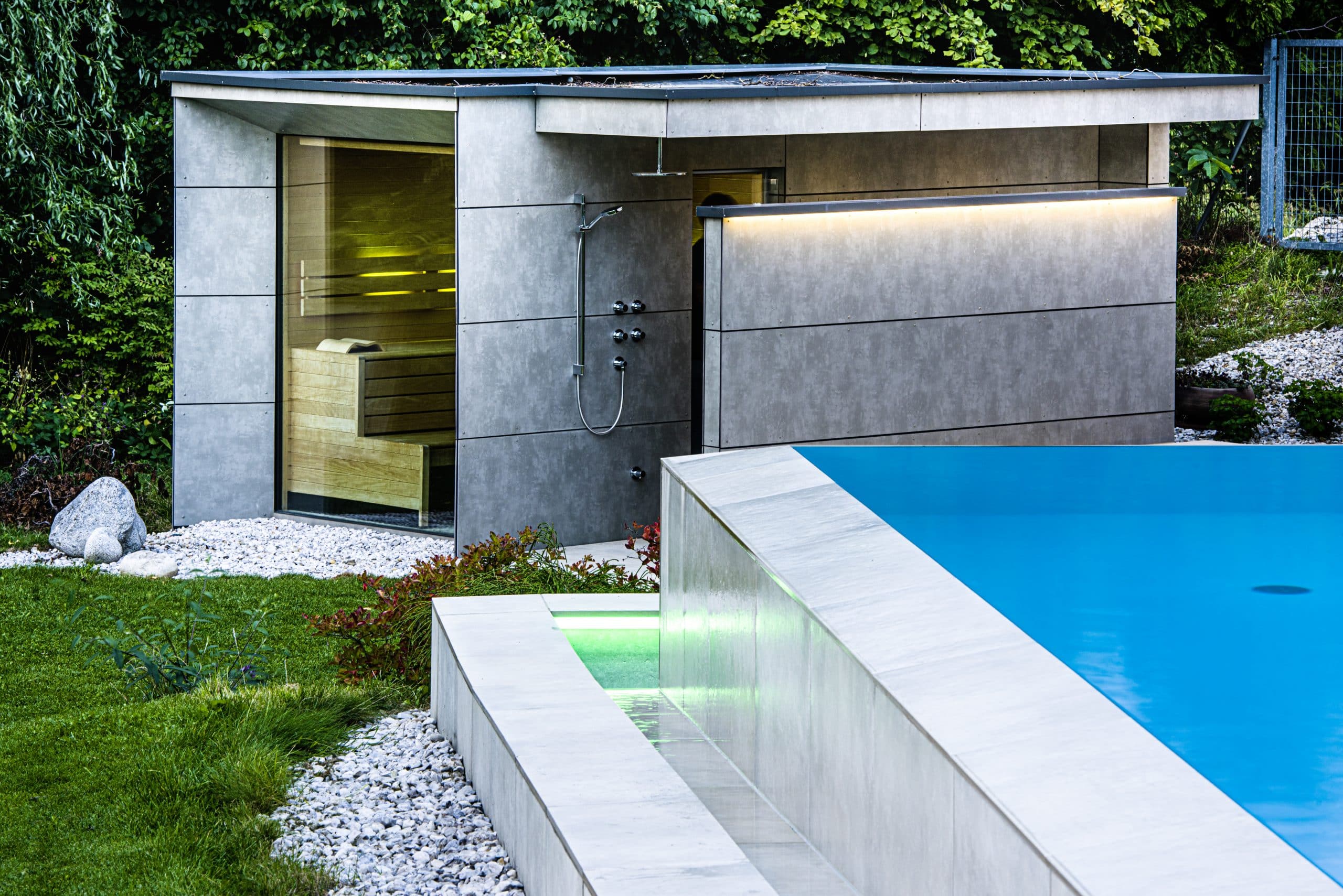 RUHA präsentiert eine Outdoorsauna mit integrierter Dusche und einen beleuchteten Pool in einem Garten.