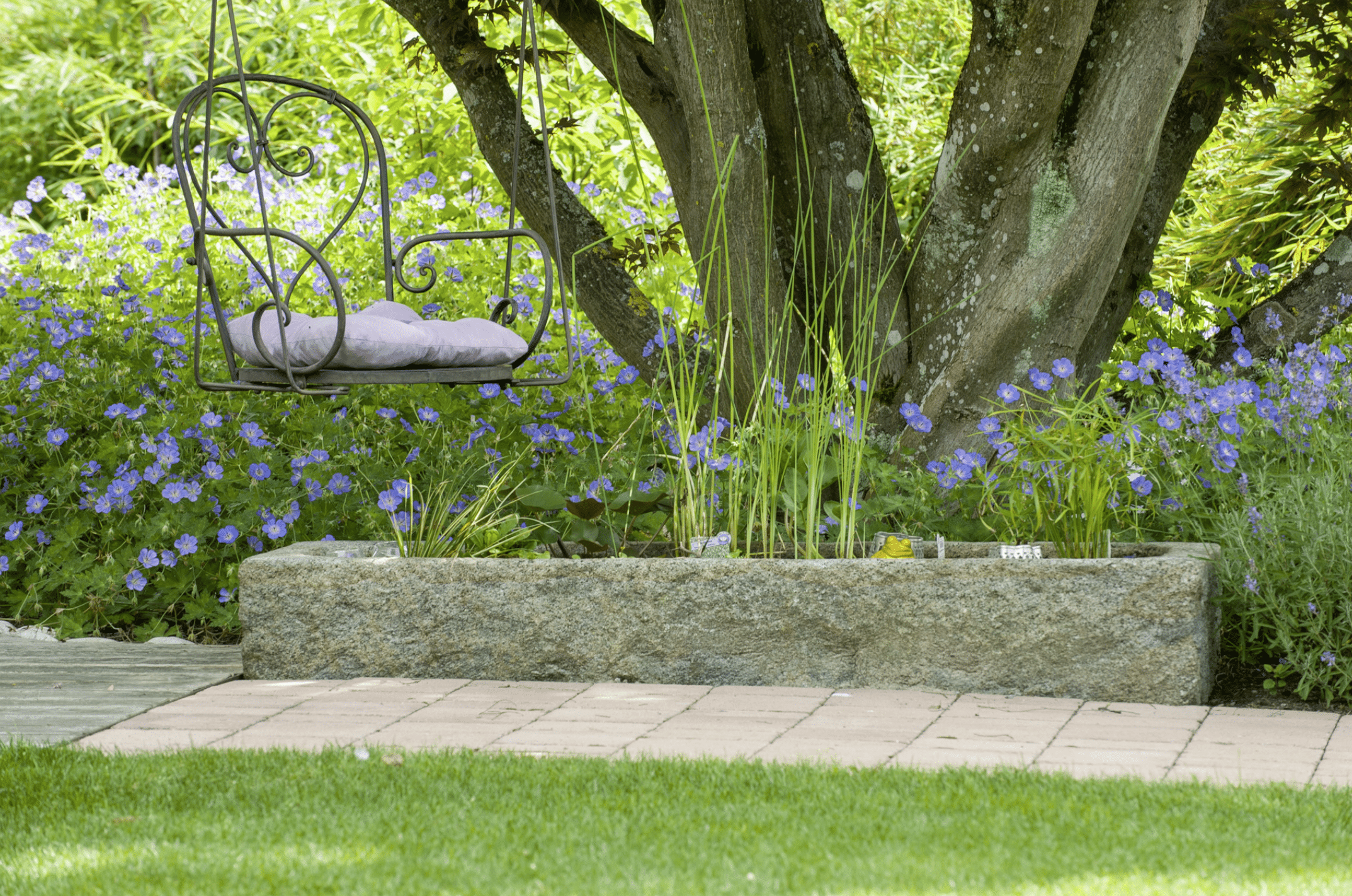 Gartenbau Schmid zeigt ein Blumenbeet aus Pflastersteinen mit weißen Blumen und Lavendel bepflanzt, Brunnen.