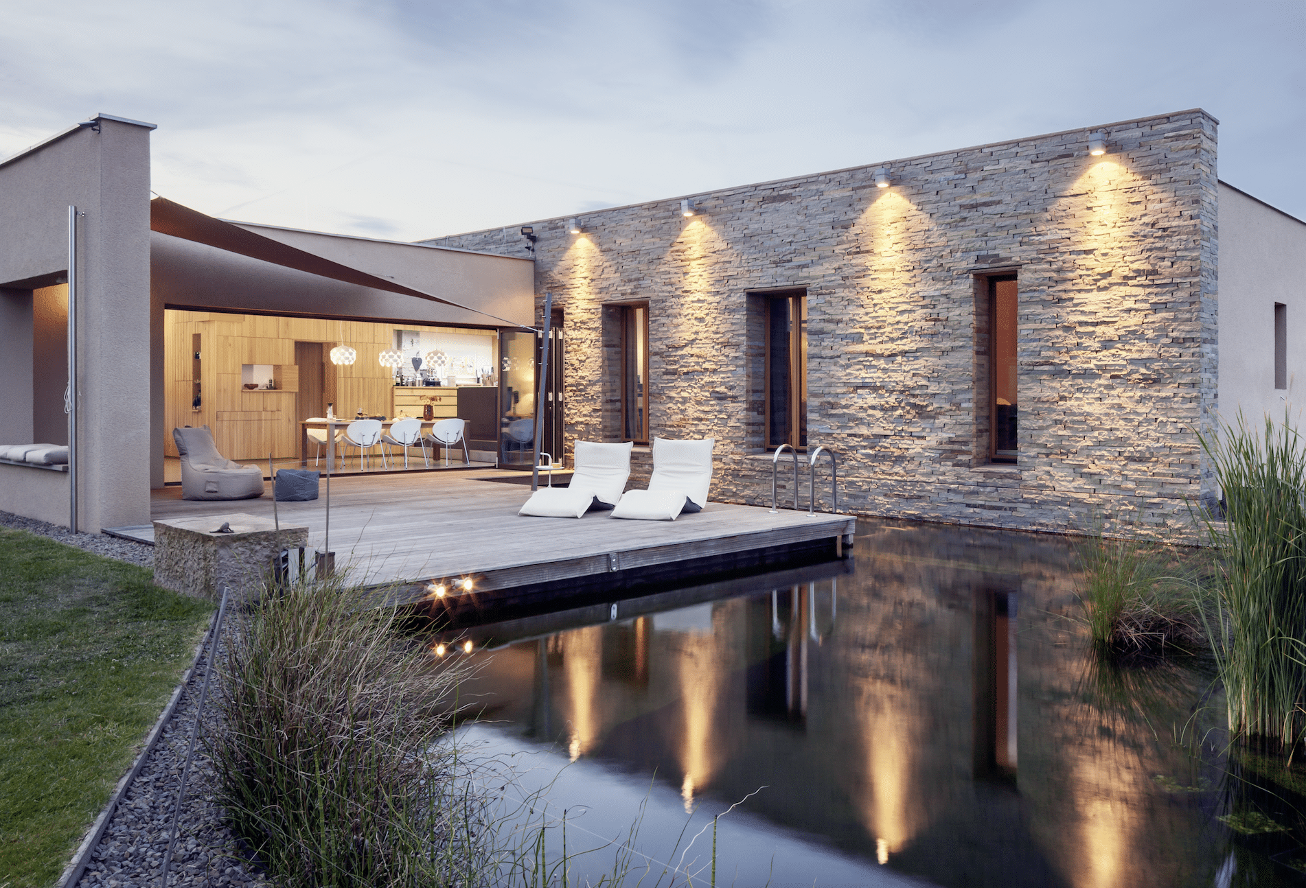 Schwimmteich mit Badedeck und modernem Haus mit Ganzglassystem von Solarlux.