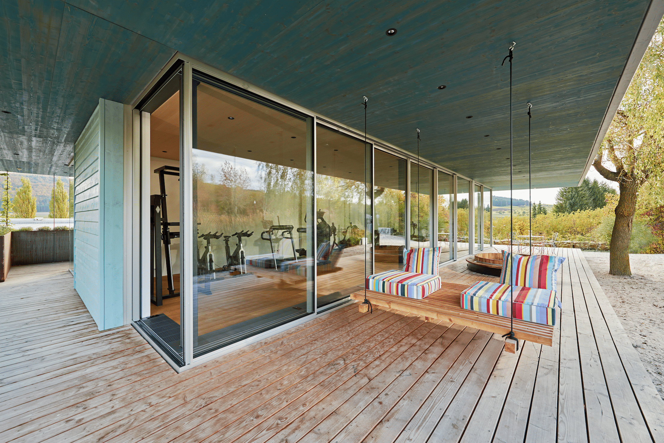Fitnesscenter mit Holz-Terrasse und Glasfront mit deckenhohen Glas-Schiebetüren von Solarlux in Wintergarten-Optik.