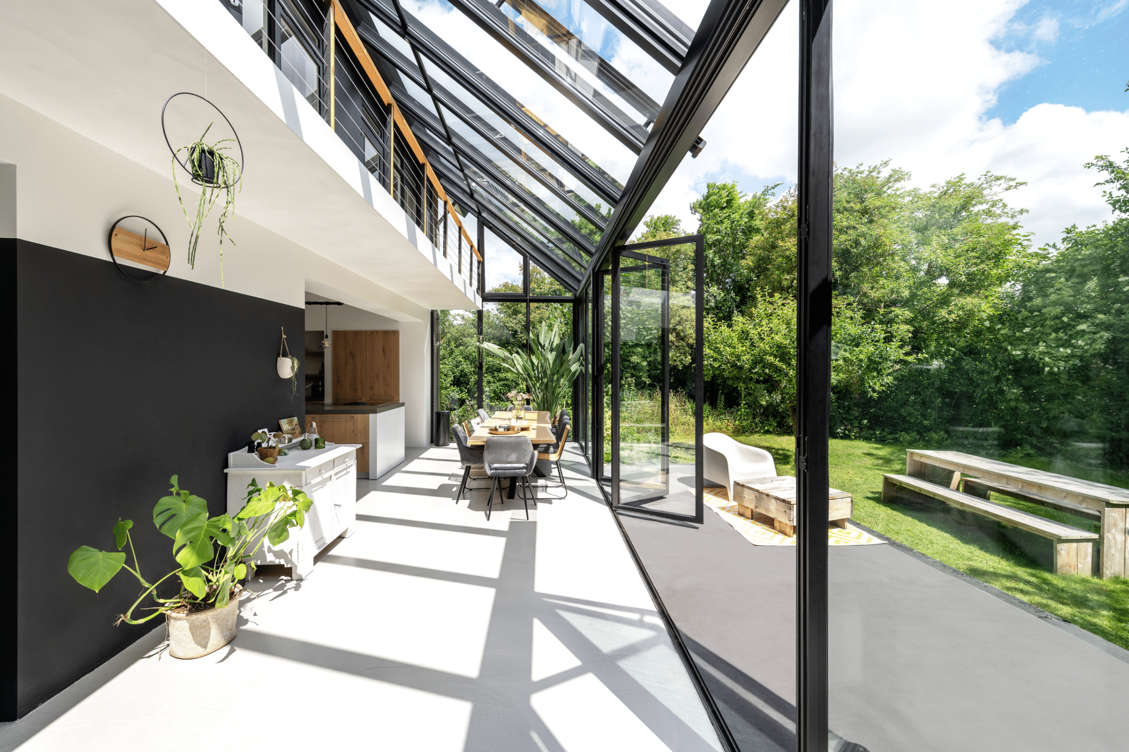 Einfamilienhaus mit zweistöckigem Wintergarten, welcher die Galerie integriert und einen Panoramablick in den Garten ermöglicht, ausgestattet mit teilweisem Glasdach und Glasfaltwänden von Solarlux.