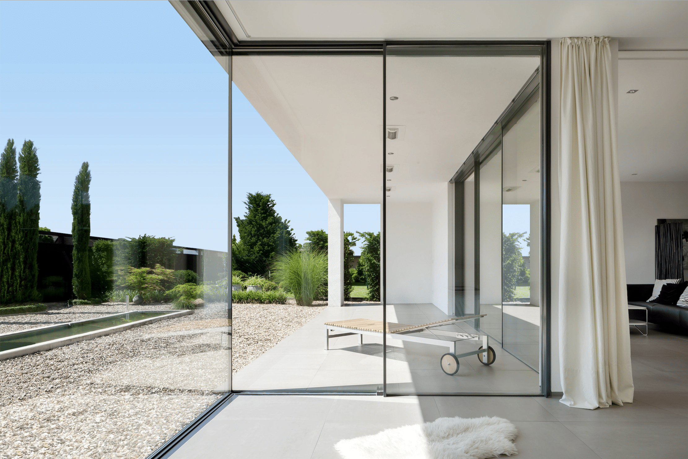 Heller, offener Raum mit deckenhoher Glasfront zur Terrasse hin, bestehend aus Glasschiebetüren von Solarlux.