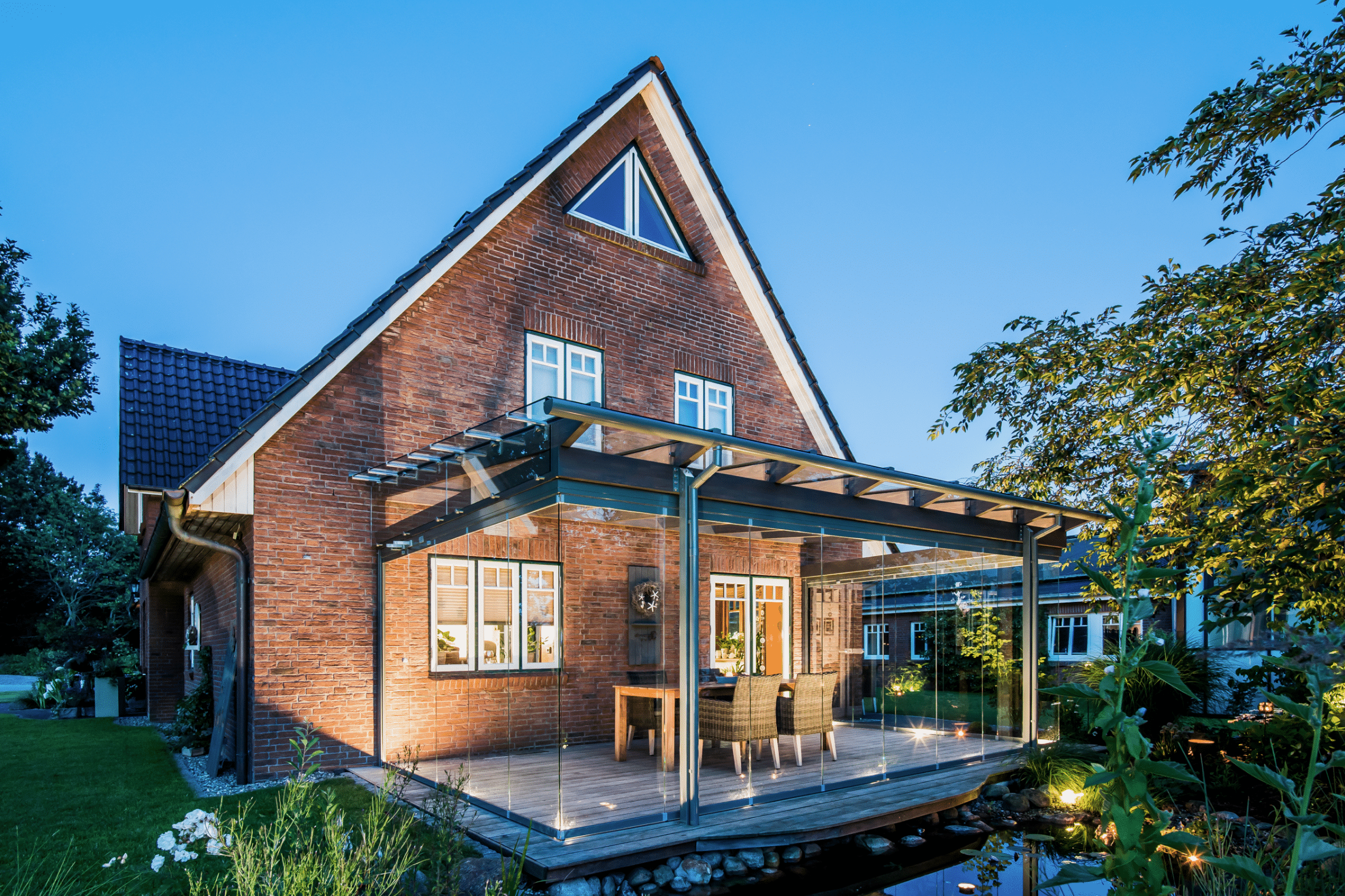 Backsteinhaus mit rundum verglaster Terrasse mit rahmenfreien Solarlux Schiebetüren und Glasdach.