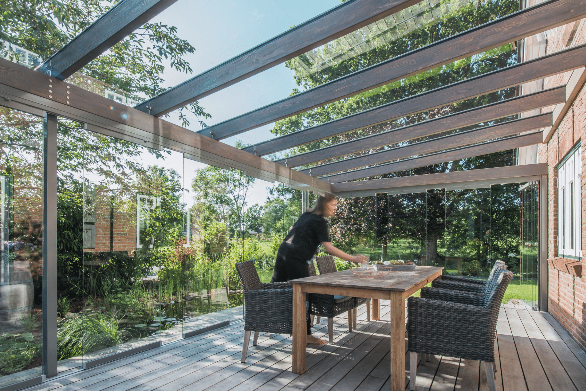 Garten mit Teich und rundum verglastem Wintergarten mit rahmenfreien Solarlux Schiebetüren und Glasdach.