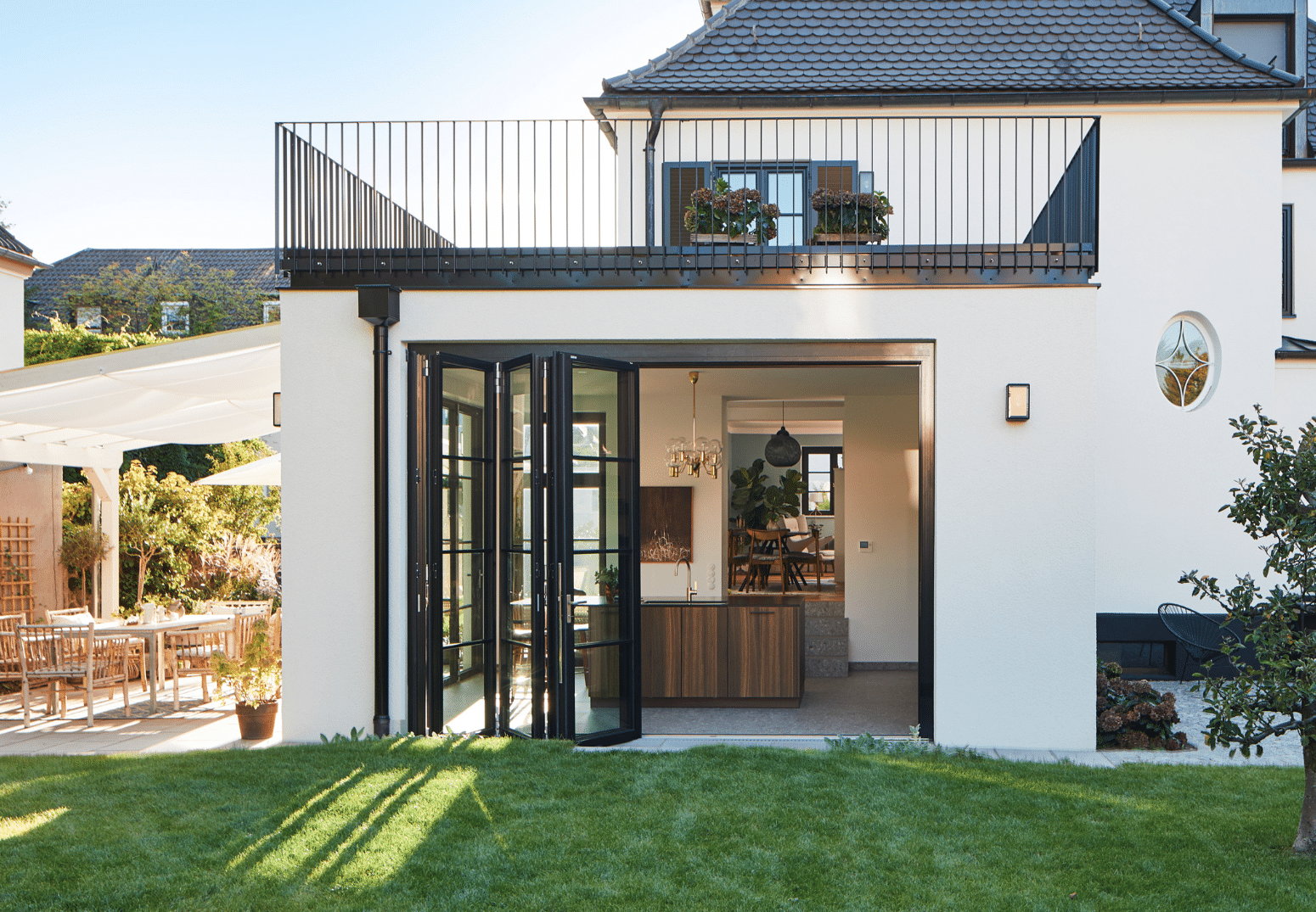 Solarlux zeigt ein Einfamilienhaus mit Balkon und Garten, ausgestattet mit Glasfalttüren im französischen Stil.