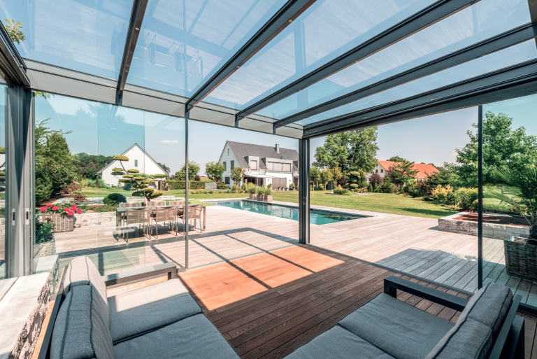 Solarlux zeigt einen Wintergarten, dessen Glaselemente sich zusammen schieben lassen und ihn so im Sommer zu einer vergrößerten Terrasse verwandeln.