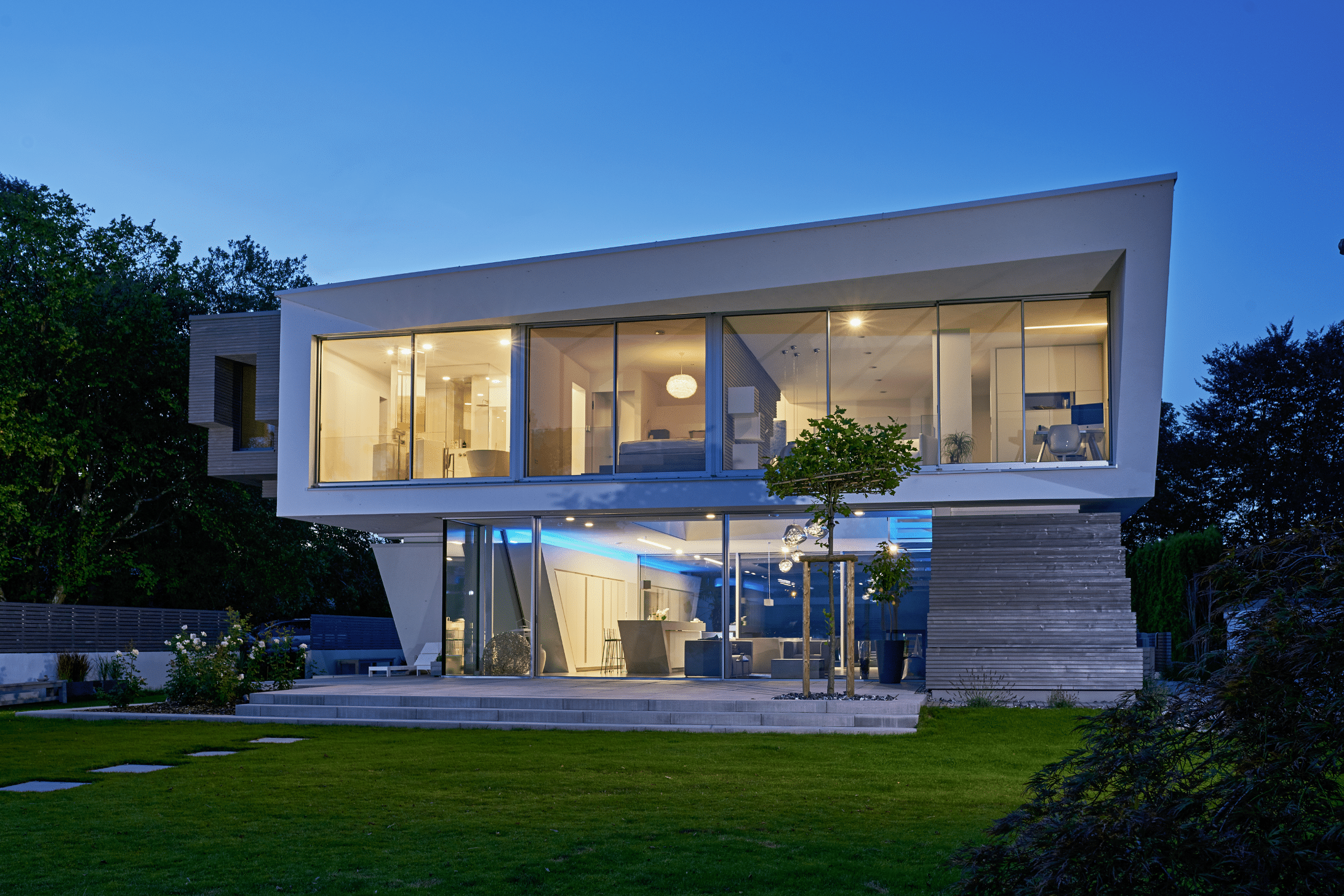 Solarlux zeigt die Villa Cero am Bodensee bei Nacht, wodurch man die blaue Beleuchtung auf der Terrasse und der Glasfaltwand gut erkennen kann.