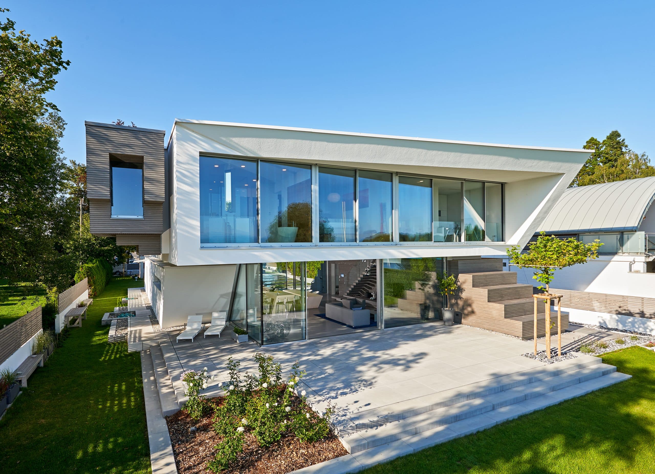 Solarlux zeigt die Villa Cero am Bodensee bei Tag, wodurch man die Fliesen und Treppe auf der Terrasse und die Glasfaltwand gut erkennen kann.