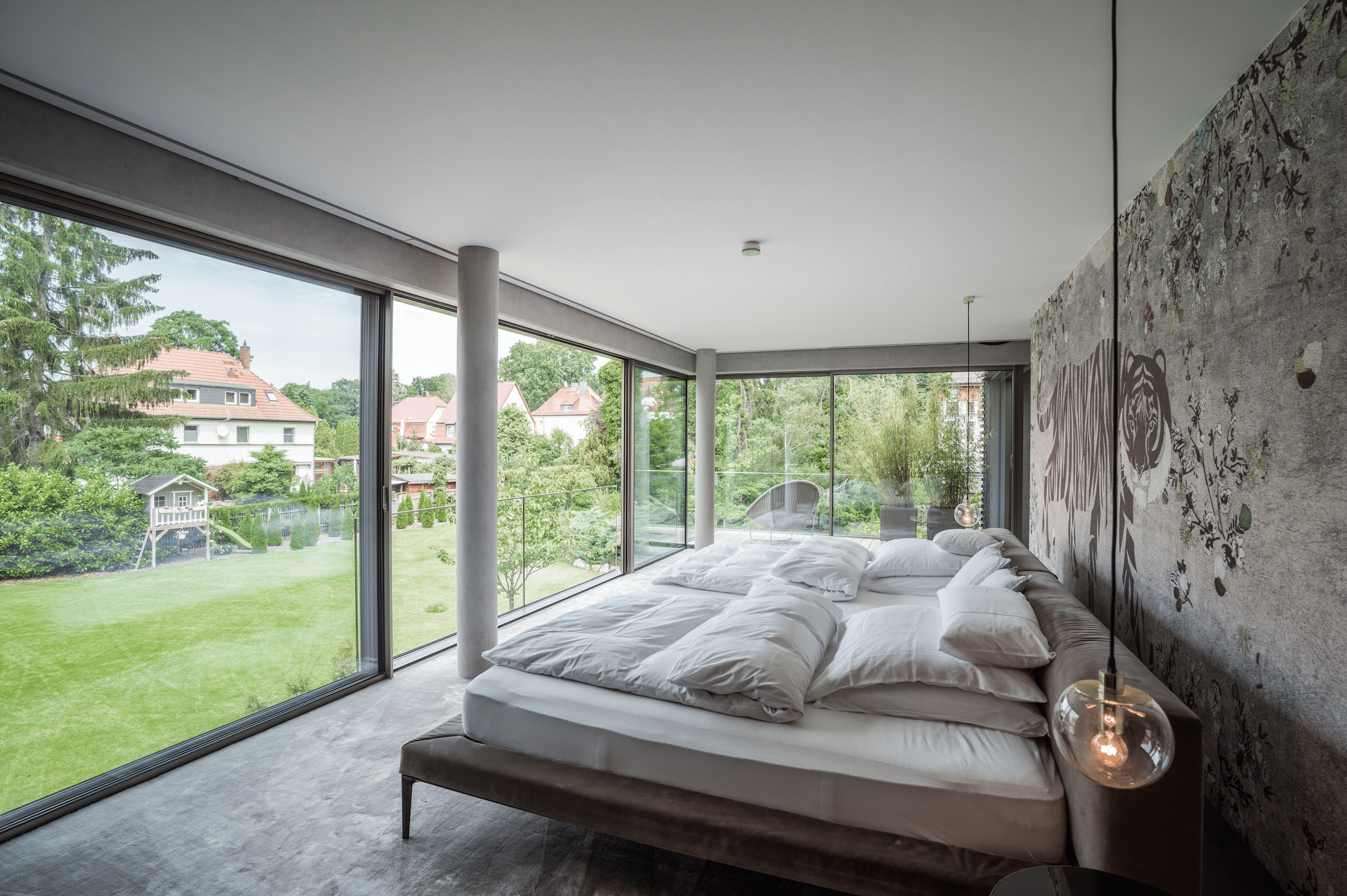Solarlux zeigt ein helles Schlafzimmer im Industrial Look mit einer gemusterten, tapezierten Wand und einer großer Fensterfront mit Aussicht in den grünen Garten.