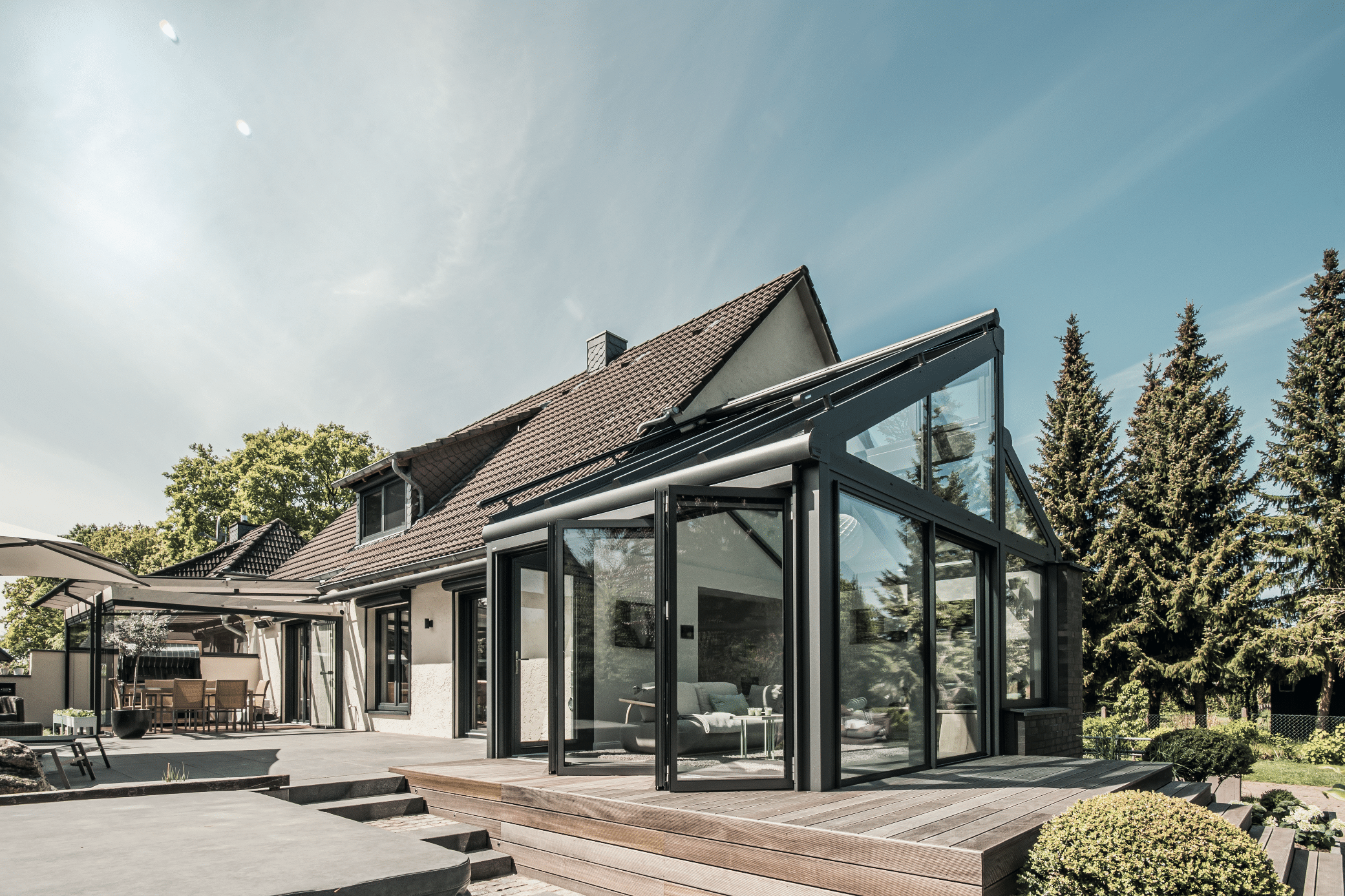 Solarlux zeigt ein Einfamilienhaus mit einer überdachten Terrasse und einen gemütlichen Wintergarten mit Zugang durch eine Glasfaltwand. © Malik Pahlmann