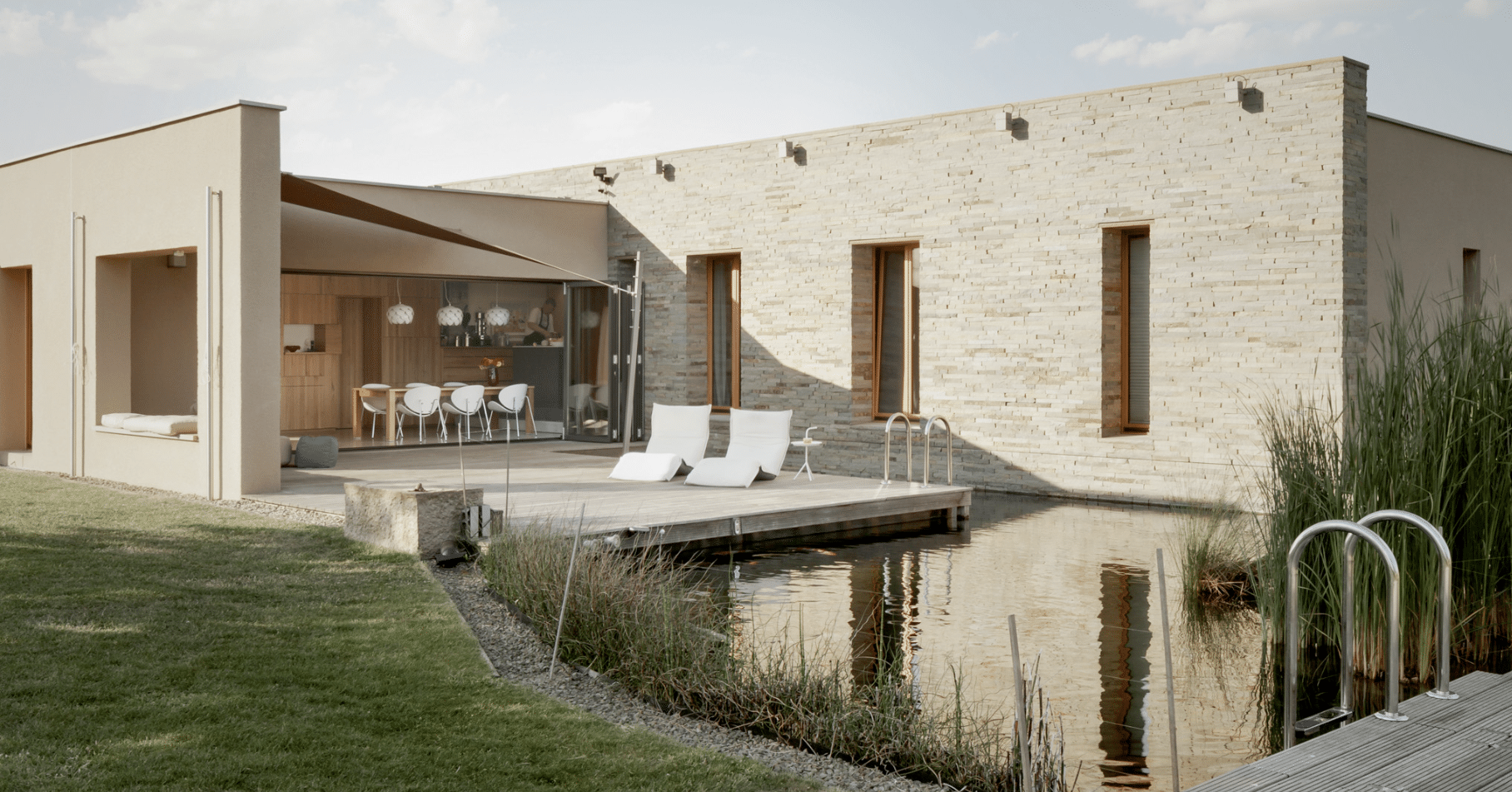 SOLARLUX präsentiert ein hoch modernes Einfamilienhaus in beige mit Naturpool, Terrasse mit Outdoormöbeln und Glasschiebetür.