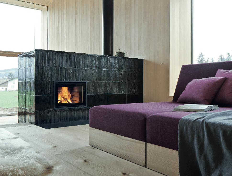Sommerhuber präsentiert ein Wohnzimmer mit lila Couch und dunkelgrauem Ofen.