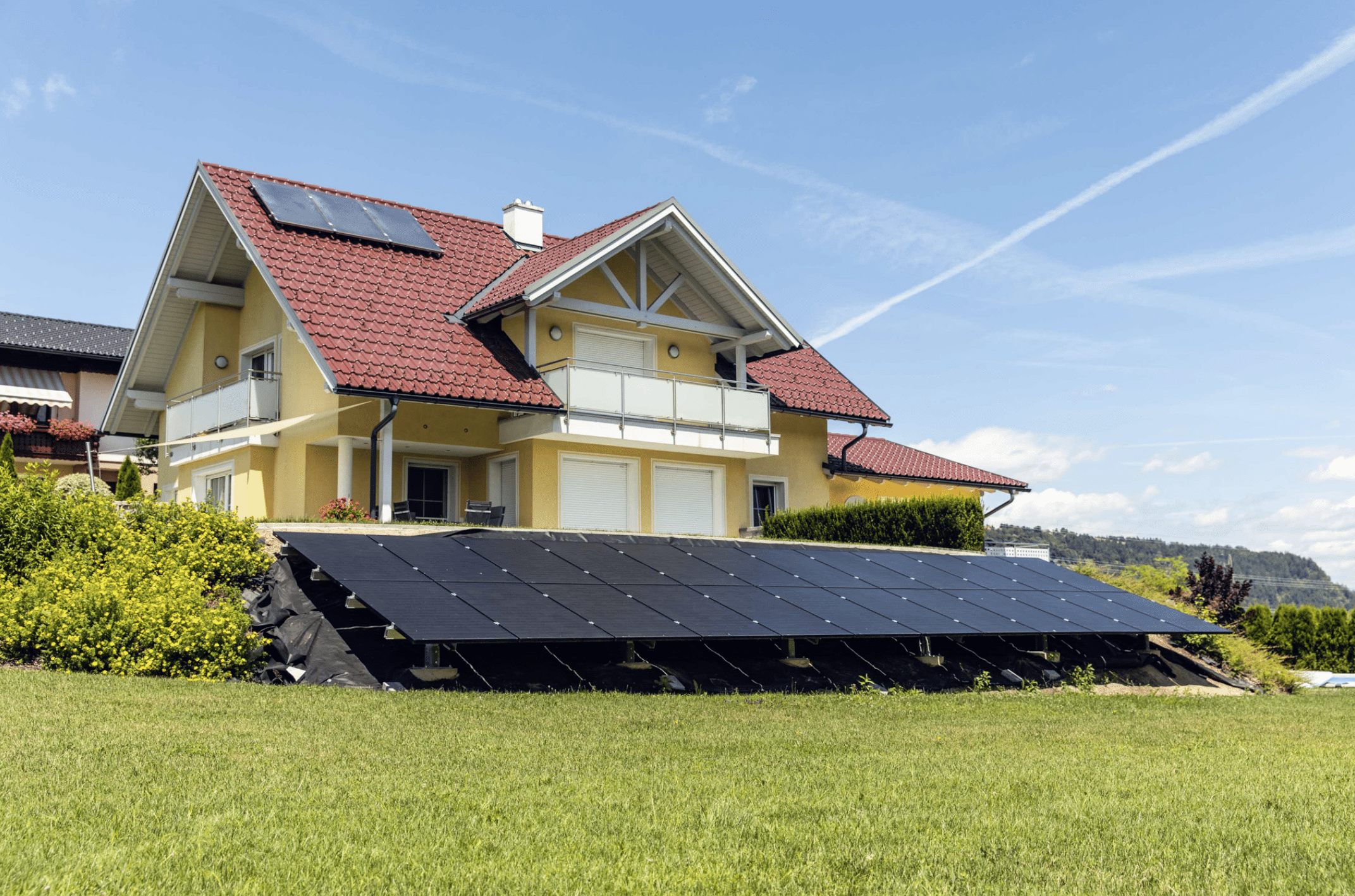 SONNENKRAFT präsentiert die Photovoltaikanlage in Hanglage eines gelben Einfamilienhauses um die Sonnen bestmöglich einzufangen.