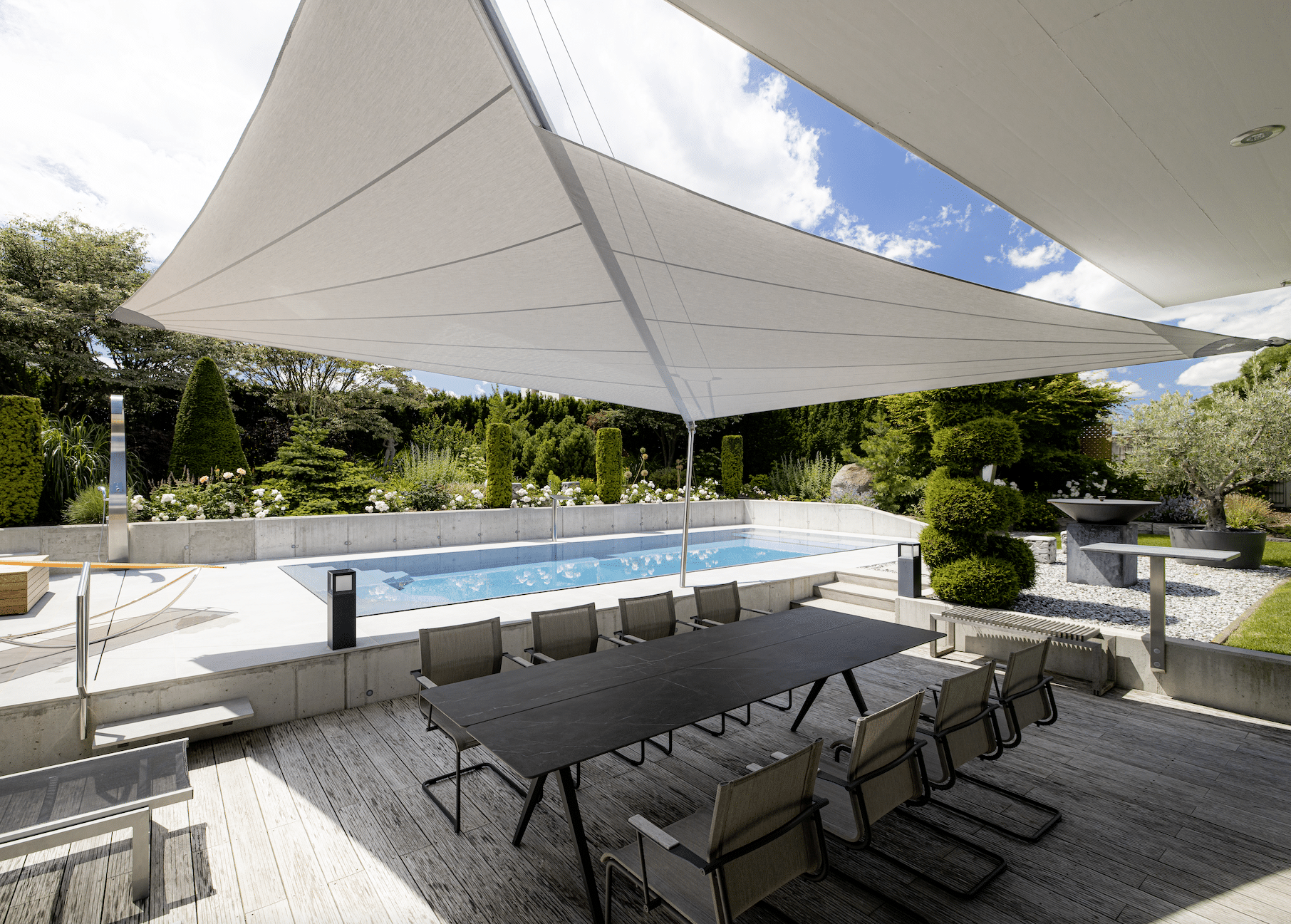Großzügiger Terrasse mit modernem Sonnensegel von SunSquare, formschönen Sitzmöglichkeiten und großem Swimmingpool im Hintergrund.