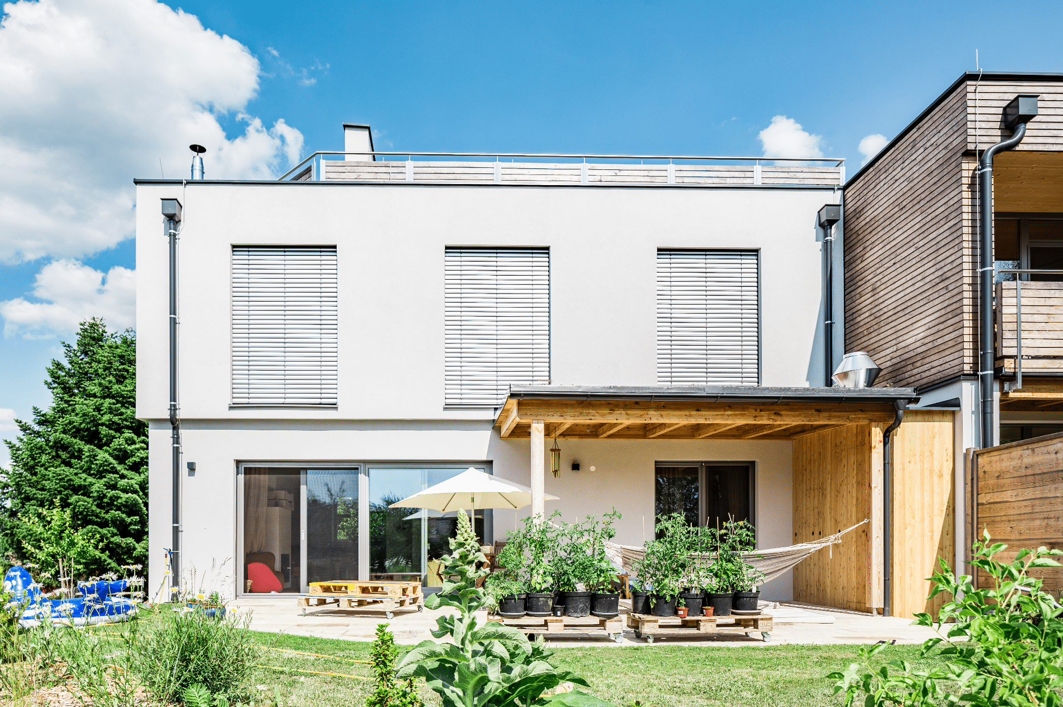 Capatect zeigt ein Einfamilienhaus mit einer überdachten Terrasse und Holzverkleidung , große Fenster mit Rollläden und einem modernen Flachdach.