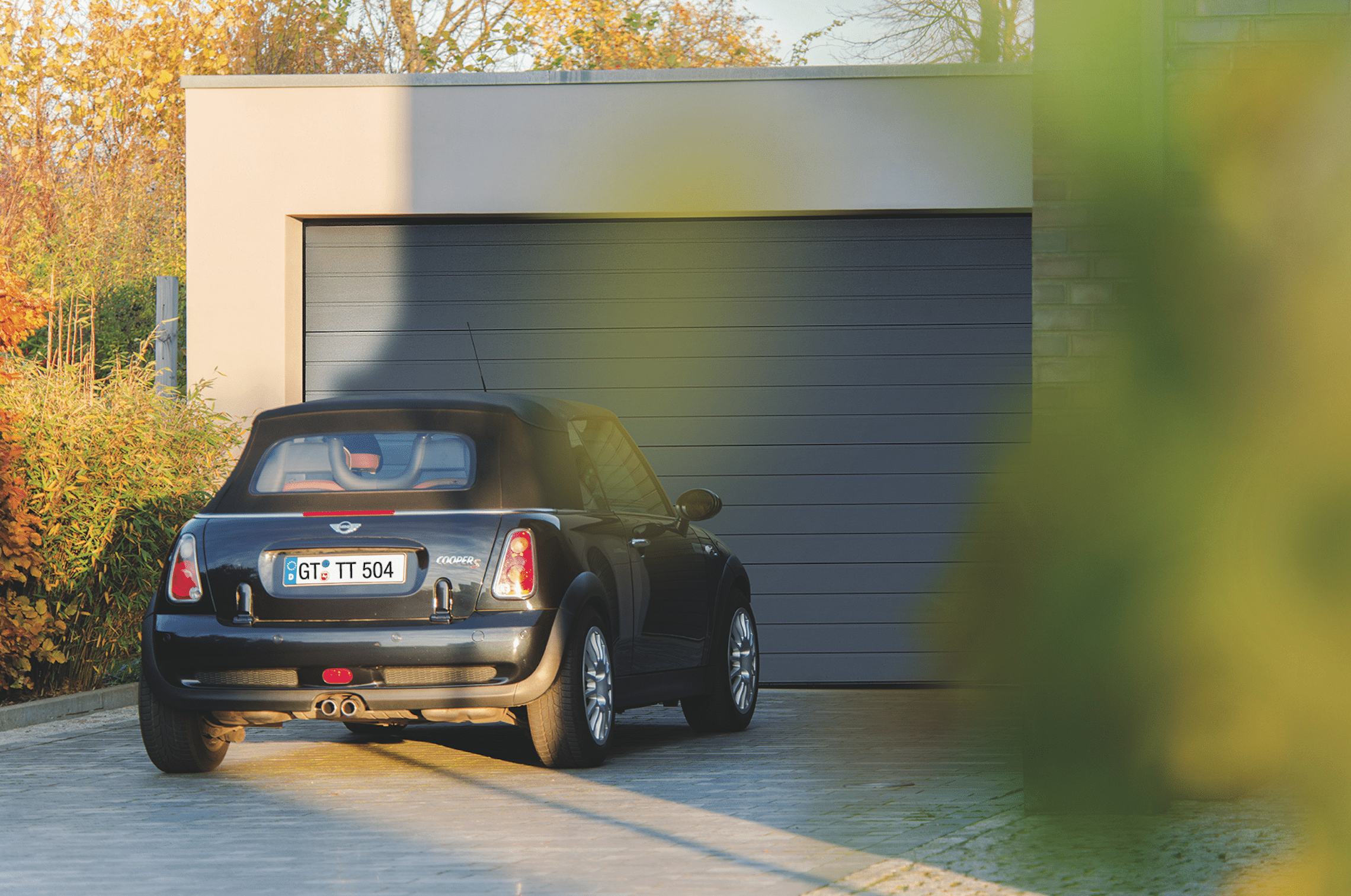 Teckentrup zeigt einen dunkelblauen Mini Cooper in der Einfahrt mit Garage, welche ei dunkelgraues Sektionaltor besitzt.