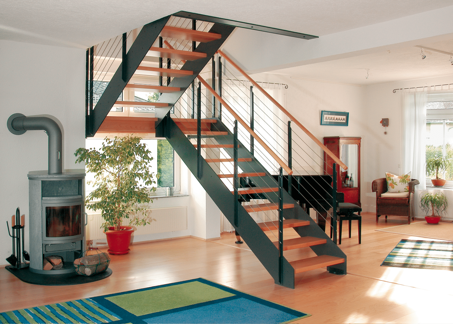 Wohnzimmer mit akzentreicher Treppe von Treppenmeister, bestehend aus Holzstufen, einem Handlauf aus Holz und einem Geländer aus gedrehten Drahtseilen, die der Stiege ihren Industrial Style verleihen.