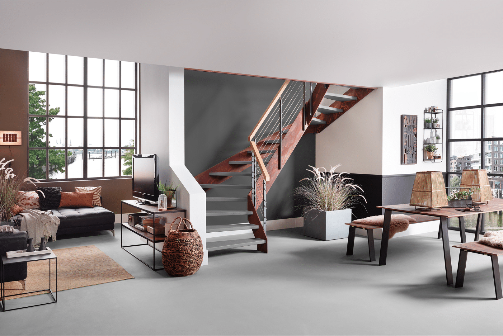 Wohnzimmer mit akzentreicher Treppe von Treppenmeister, bestehend aus grauen Stufen, einem Handlauf aus Holz und einem rostig anmutendem Gerüst, welches der Stiege ihren Industrial Look verleiht.