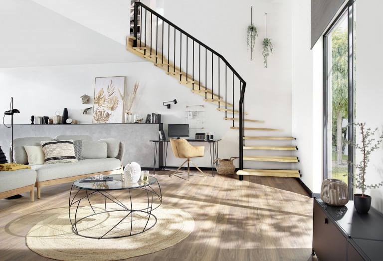 Treppenmeister zeigt ein modernes Wohnzimmer mit Blick in den Garten und einer Faltwerktreppe mit Flachstahlgeländer aus dunklem Holz, als Aufgang in den oberen Stock.