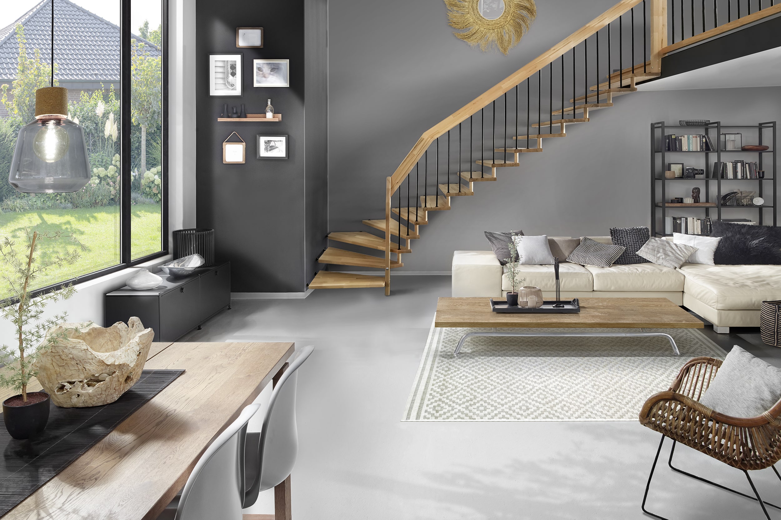 Treppenmeister zeigt ein modernes Wohnzimmer in grau, mit einem Essbereich, einer hellen Couch und Beistelltisch aus Holz, einem Panoramafenster und Holztreppe.