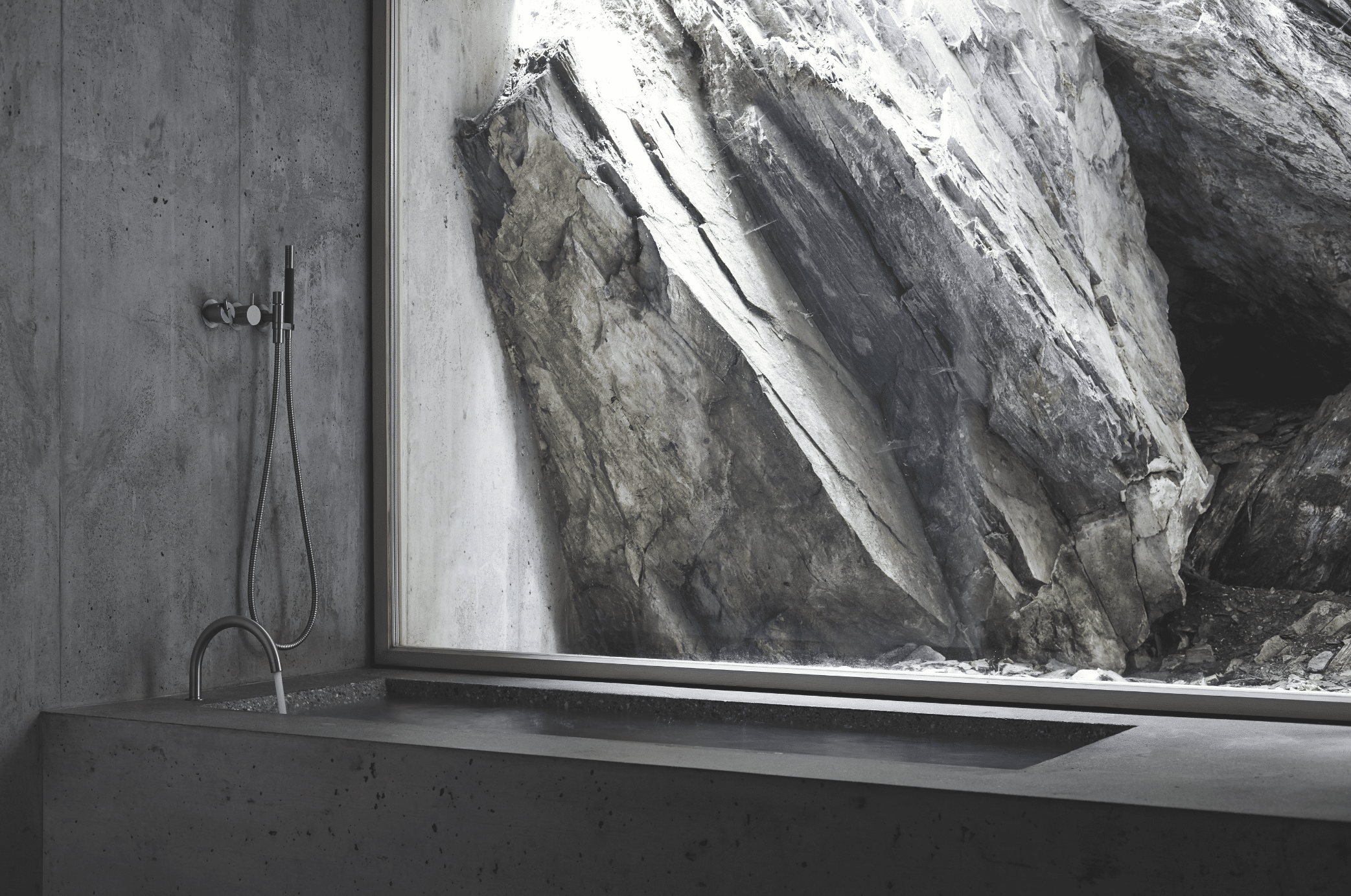 VOLA zeigt eine graue Badewanne mit silbernen Armaturen neben einem großen Fenster und Blick auf Gebirge.