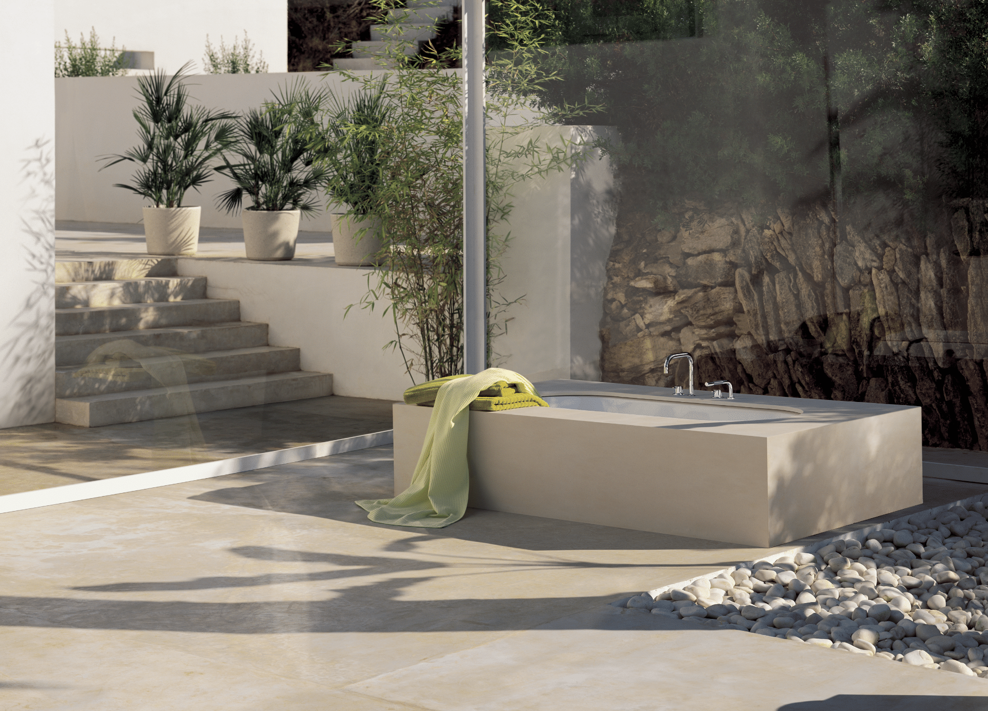 VOLA zeigt einen Garten mit gefliester Terrasse und Outdoor-Badewanne in beige mit silbernen Armaturen.