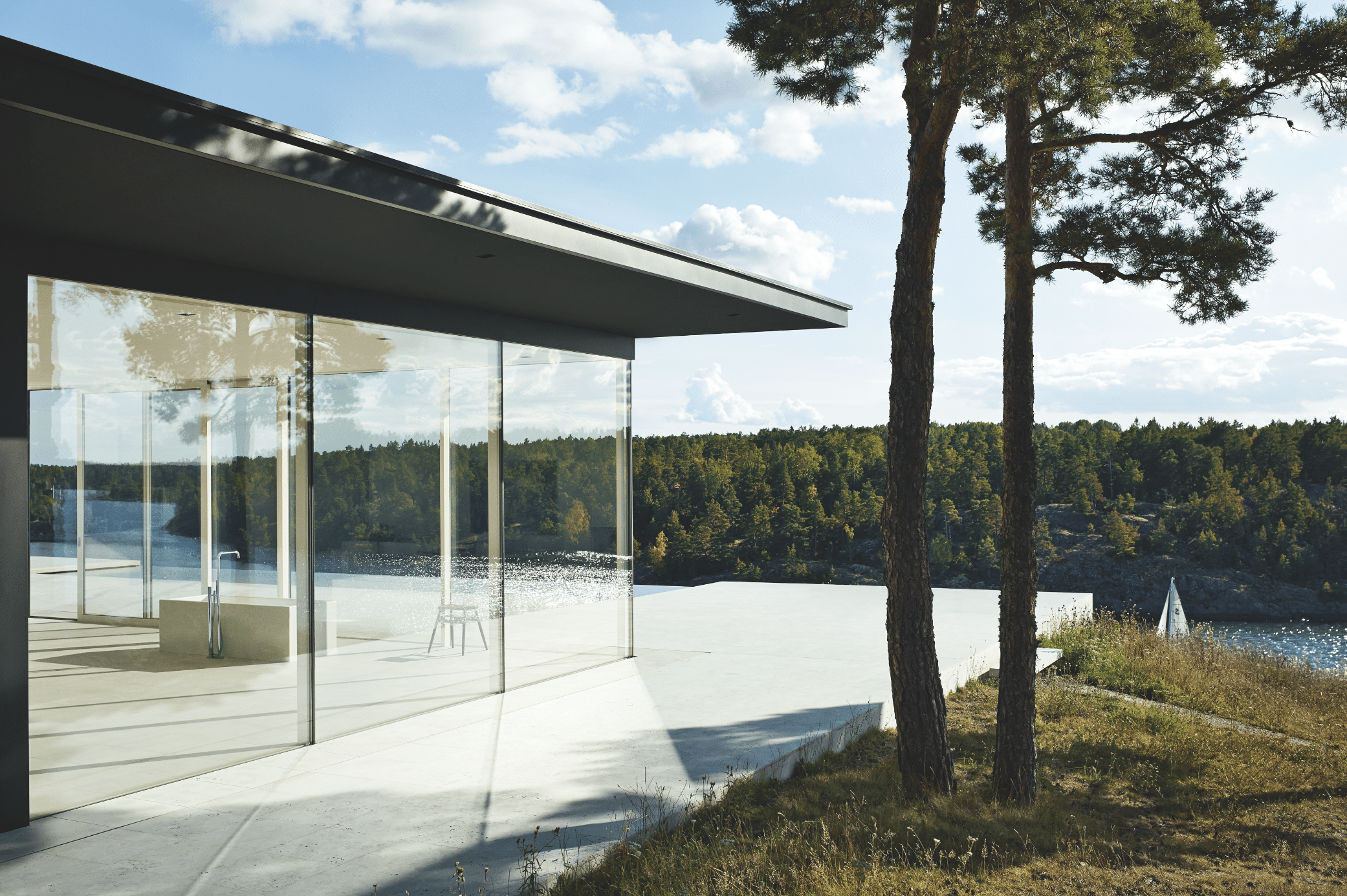 VOLA zeigt ein Ferienhaus mit Glaswänden und einer freistehenden Badewanne mit Blick in den Wald.
