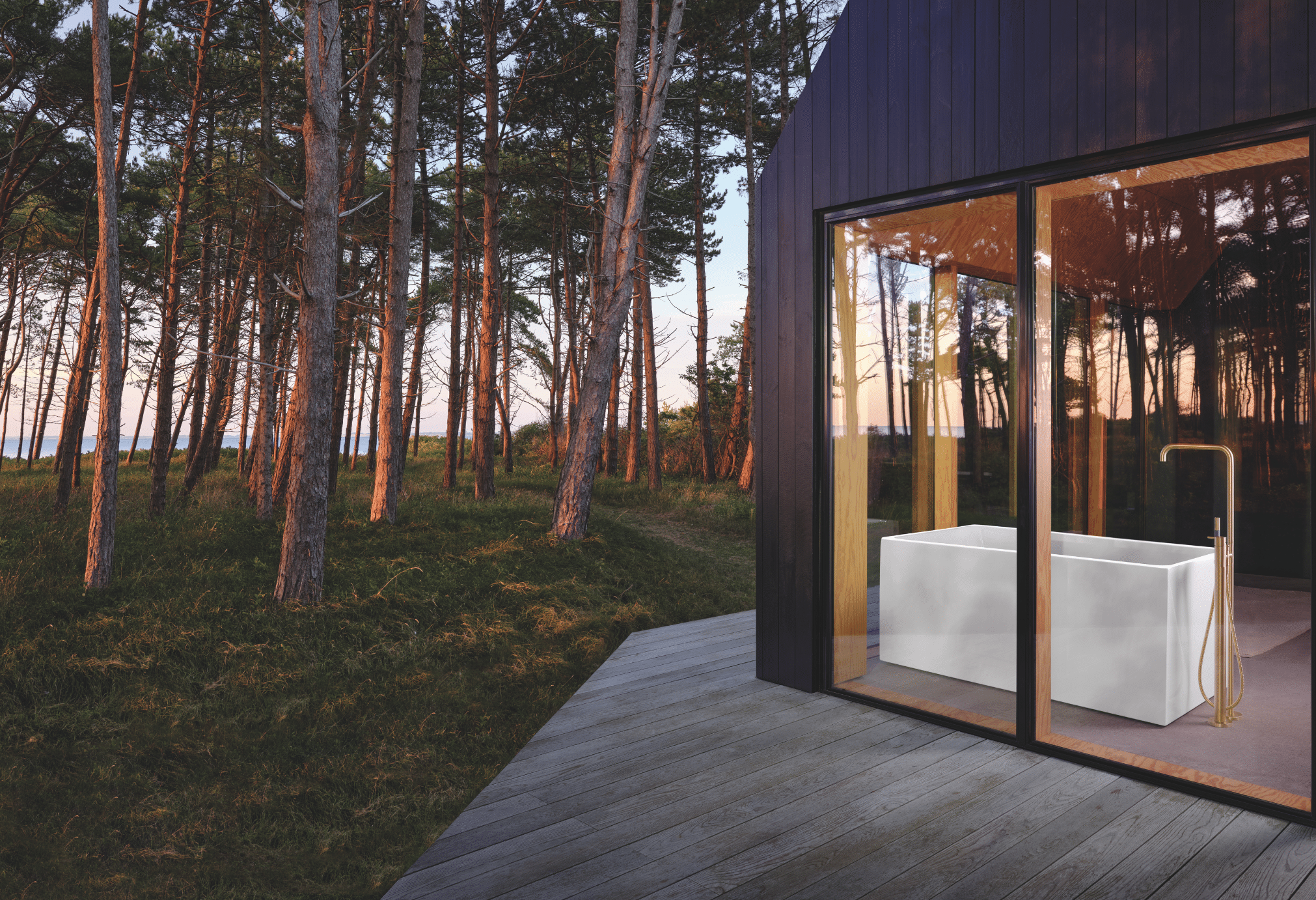 VOLA zeigt eine Waldhütte aus Holz mit großen Fenstern und einer freistehenden Badewanne mit goldenen Armaturen.