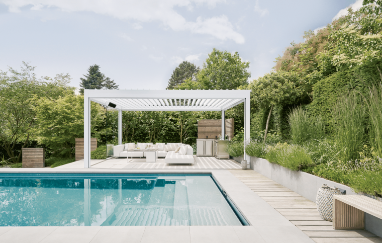 Warema zeigt Garten mit Pool und weißer Pergola mit Outdoorküche und weißer Outdoor-Eck-Lounge.