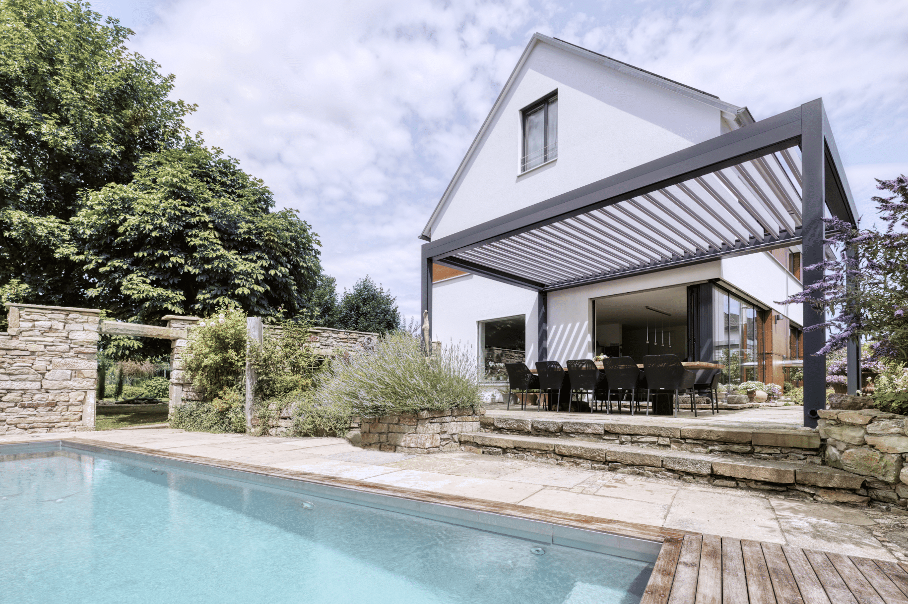 Modernes Einfamilienhaus mit mediteranem Garten mit Pool und Terrasse, die mit einem Lamellendach Lamaxa L70 von WAREMA beschattet wird.