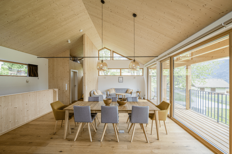 Blick in den offenen Wohnraum mit Essbereich, Sofalandschaft und Wand- und Deckenverkleidung aus Holz von Weissenseer Holz-System-Bau.