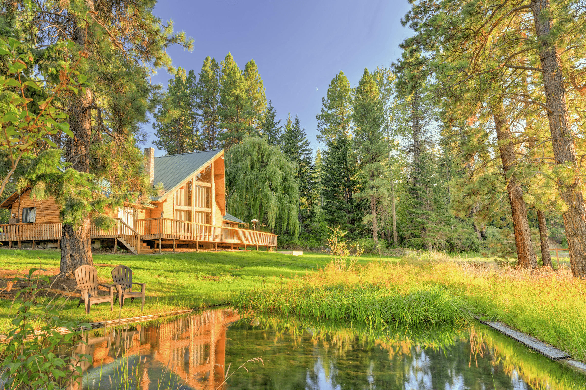 Holzblockhaus mit grünem Metalldach auf großem Grundstück in naturbelassender Landschaft.