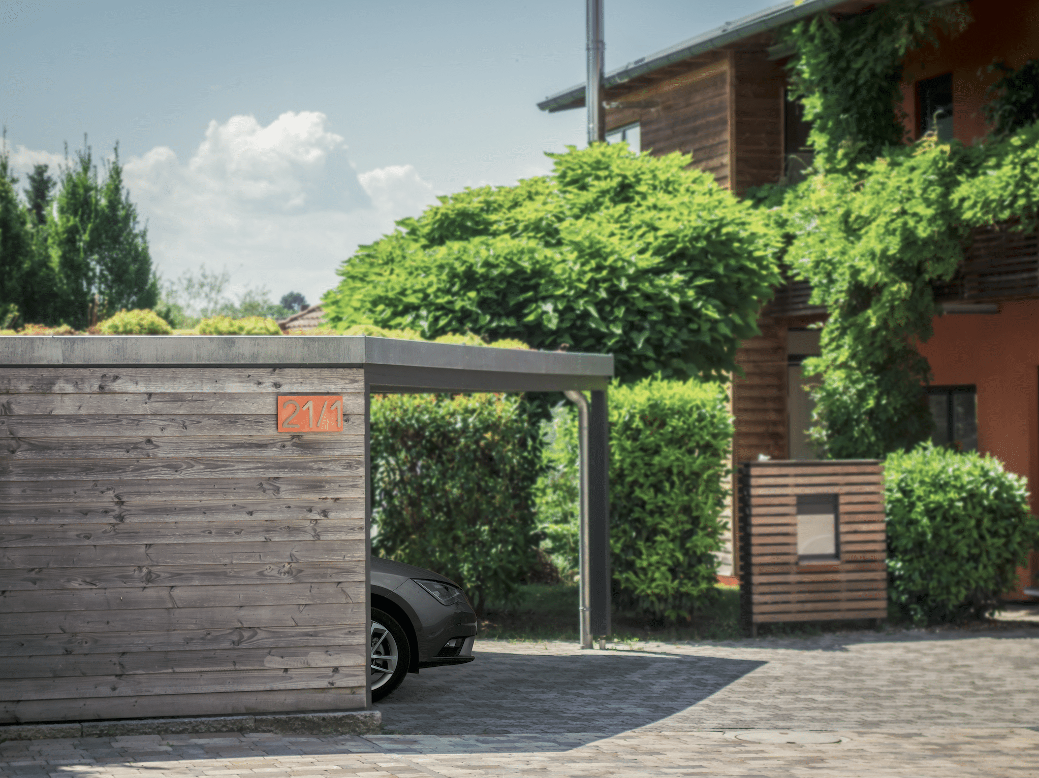 Modernes Carport aus Holz mit darin geparktem Auto vor einem Wohnhaus.